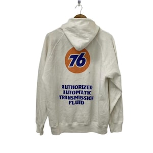 Puede incluir: Sudadera con capucha blanca con un gran c&iacute;rculo naranja que contiene el n&uacute;mero 76 en azul. El texto "AUTHORIZED AUTOMATIC TRANSMISSION FLUID" est&aacute; impreso en azul debajo del c&iacute;rculo.