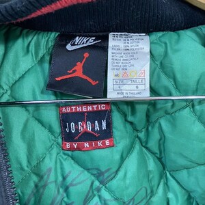 Pu&ograve; includere: Una giacca reversibile nera e verde con un colletto rosso e nero. La giacca ha una chiusura a zip e una grande toppa "Authentic Jordan by Nike" sul davanti. La fodera &egrave; verde e ha un motivo trapuntato. L'etichetta sulla giacca dice "Taglia L, Taille G, Prodotto in Thailandia".