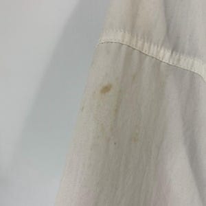 Pu&ograve; includere: Primo piano di una camicia di cotone bianca con alcune macchie di colore marrone chiaro.