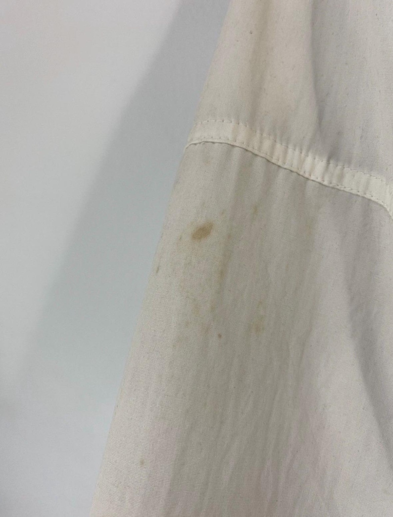 Pu&ograve; includere: Primo piano di una camicia di cotone bianca con alcune macchie di colore marrone chiaro.