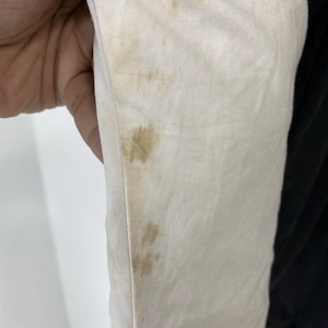 Pu&ograve; includere: Primo piano di un tessuto bianco con macchie marroni. Il tessuto &egrave; piegato e sembra far parte di un capo di abbigliamento.