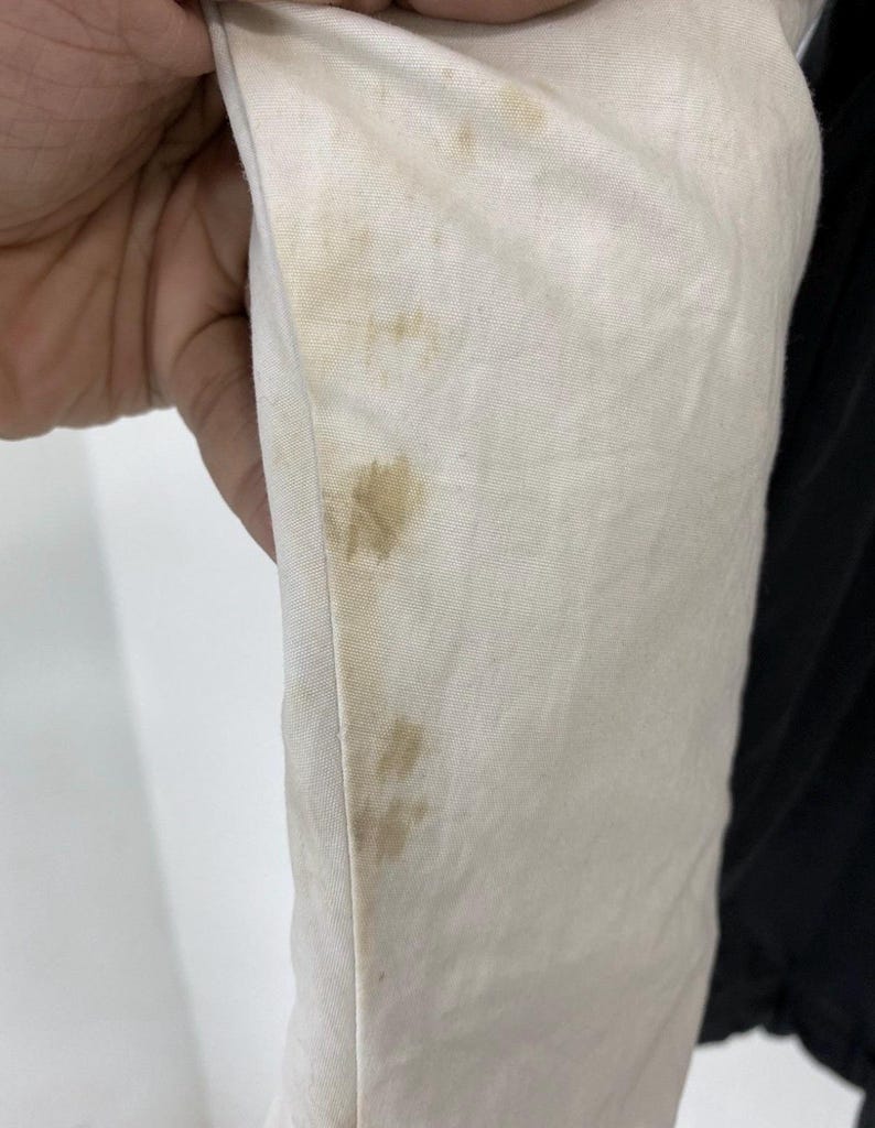 Pu&ograve; includere: Primo piano di un tessuto bianco con macchie marroni. Il tessuto &egrave; piegato e sembra far parte di un capo di abbigliamento.