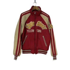 Peut inclure: Veste de baseball rouge et crème avec un texte brodé jaune et blanc qui dit "Chute Shock Yellow Corn" et un petit patch jaune et blanc qui dit "Yellow Corn".