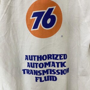 Puede incluir: Sudadera blanca con un gran c&iacute;rculo naranja que contiene el n&uacute;mero 76 en azul. Debajo del c&iacute;rculo est&aacute; el texto "AUTHORIZED AUTOMATIC TRANSMISSION FLUID" en azul.