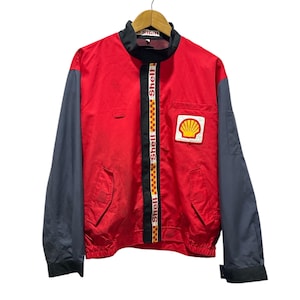 May include: A red and black jacket with a Shell logo on the pocket and the word "Shell" repeated down the zipper. The jacket has a black and white checkered stripe down the zipper.