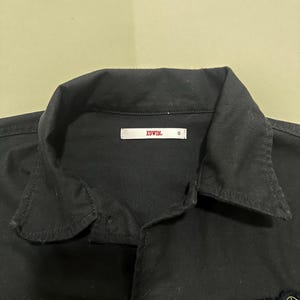 Pode incluir: Camisa preta abotoada com gola e patches bordados. A camisa tem uma etiqueta que diz "EDWIN" e o tamanho "S". A camisa &eacute; feita de um material resistente e tem um design cl&aacute;ssico.