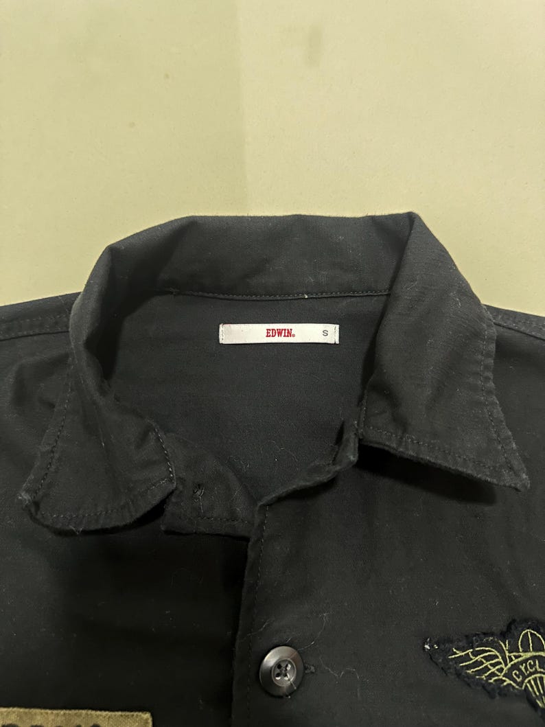 Pode incluir: Camisa preta abotoada com gola e patches bordados. A camisa tem uma etiqueta que diz "EDWIN" e o tamanho "S". A camisa &eacute; feita de um material resistente e tem um design cl&aacute;ssico.