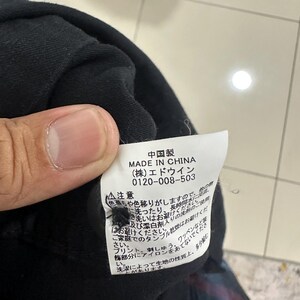 Pode incluir: Uma pe&ccedil;a de roupa preta com uma etiqueta branca com texto japon&ecirc;s e as palavras "MADE IN CHINA". A etiqueta tamb&eacute;m inclui um n&uacute;mero de telefone e instru&ccedil;&otilde;es de cuidados. A pe&ccedil;a de roupa &eacute; segurada por uma pessoa.