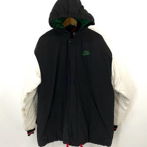 Pu&ograve; includere: Giacca con cappuccio nera e bianca con un logo Nike verde sul davanti. La giacca ha una manica bianca e un cordoncino rosso.