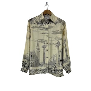 Könnte beinhalten: Cremefarbenes Button-Down-Hemd mit einem schwarz-weißen Architektur-Print. Das langärmlige Hemd zeigt eine detaillierte Illustration einer Stadtlandschaft mit Säulen und Figuren. Der Kragen trägt den Markennamen "MOSCHINO".