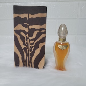 May include: A vintage perfume bottle with a clear, ornate stopper and a gold label that reads "Vol de Nuit Guerlain." The bottle contains a golden-colored liquid and sits next to a brown box with a zebra stripe pattern.