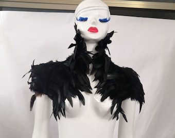 May include: Black feather shoulder piece with a matching feather collar. The collar is worn around the neck and the shoulder piece is worn on one shoulder.