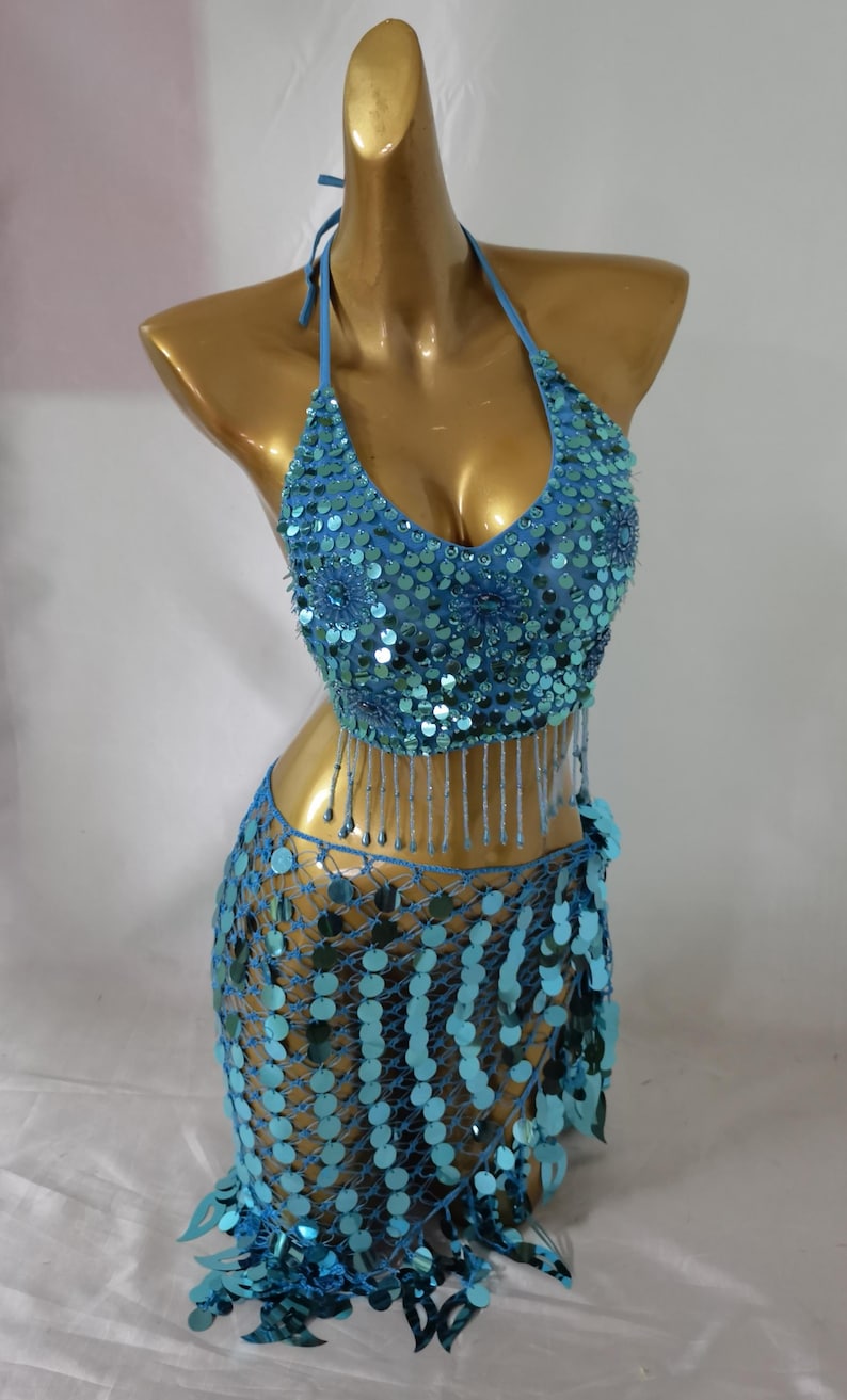 May include: A turquoise blue sequined belly dancing costume with a halter top and a skirt with fringe. The top and skirt are both covered in sequins and beads.