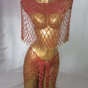 May include: A red and gold beaded costume set. The set includes a beaded top with a net-like design and a matching skirt. The costume is displayed on a mannequin. The beads are gold and the fabric is red.