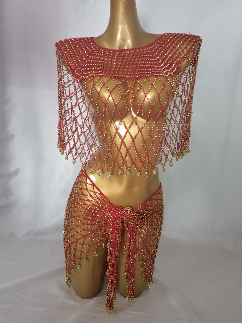 May include: A red and gold beaded costume set. The set includes a beaded top with a net-like design and a matching skirt. The costume is displayed on a mannequin. The beads are gold and the fabric is red.