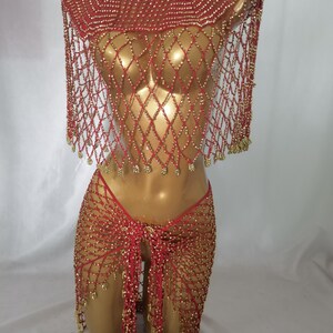May include: A red beaded outfit on a mannequin. The outfit includes a top with a round neckline and a diamond-patterned net design, a matching skirt, and a thong. Gold beads are interspersed throughout the red netting.