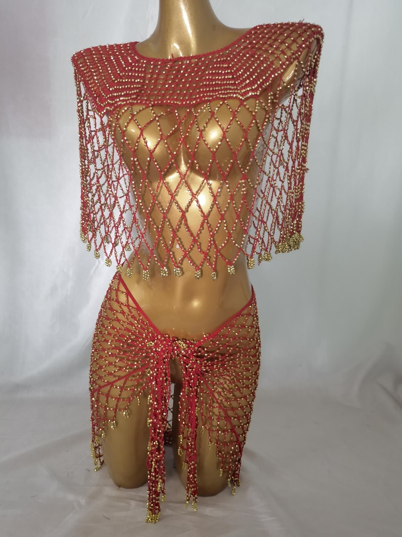 May include: A red beaded outfit on a mannequin. The outfit includes a top with a round neckline and a diamond-patterned net design, a matching skirt, and a thong. Gold beads are interspersed throughout the red netting.