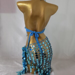 May include: A blue sequined halter top and skirt set with a mesh design. The top has a halter neck and ties at the back. The skirt is a short, flowing skirt with a fringe hem.