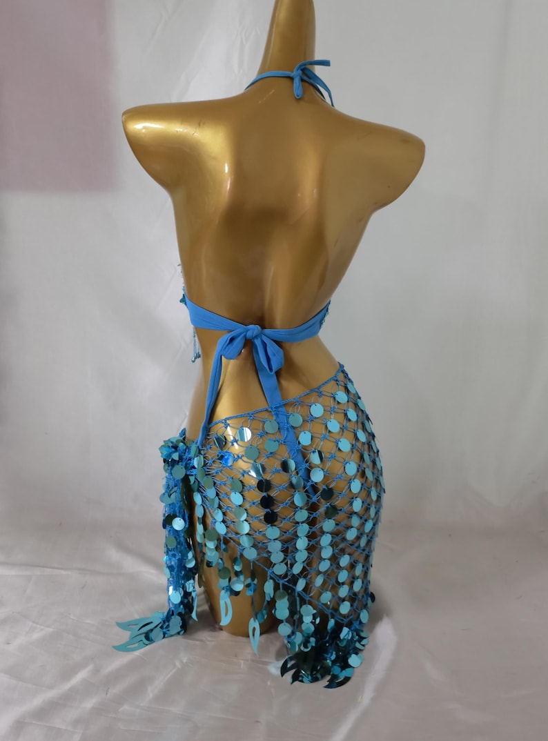 May include: A blue sequined halter top and skirt set with a mesh design. The top has a halter neck and ties at the back. The skirt is a short, flowing skirt with a fringe hem.