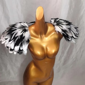 Puede incluir: Un par de hombreras de plumas negras y blancas con pedrer&iacute;a. Las hombreras est&aacute;n hechas de plumas y est&aacute;n unidas a una banda el&aacute;stica transparente.