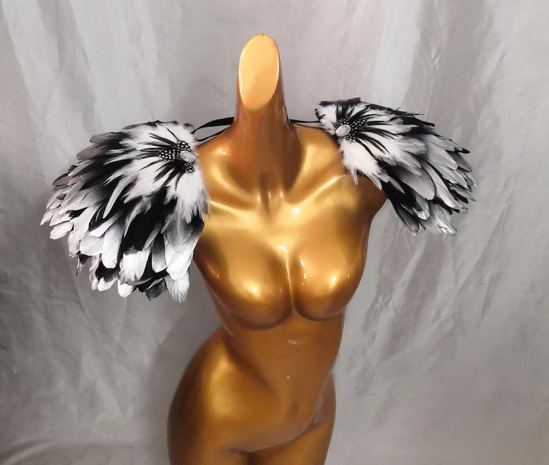 Puede incluir: Un par de hombreras de plumas negras y blancas con pedrer&iacute;a. Las hombreras est&aacute;n hechas de plumas y est&aacute;n unidas a una banda el&aacute;stica transparente.