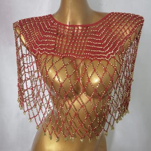 May include: A red and gold beaded shoulder wrap displayed on a mannequin. The wrap has a net-like design with gold beads at the intersections and edges. This decorative accessory is a shoulder wrap.