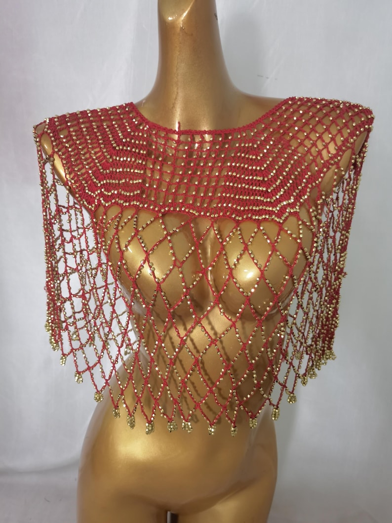 May include: A red and gold beaded shoulder wrap displayed on a mannequin. The wrap has a net-like design with gold beads at the intersections and edges. This decorative accessory is a shoulder wrap.
