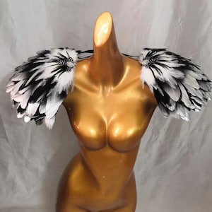 Puede incluir: Un par de hombreras de plumas negras y blancas con pedrer&iacute;a. Las hombreras se llevan sobre un maniqu&iacute; con un cuerpo de color dorado.