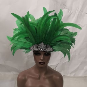 Peut inclure: Une coiffe de plumes vertes avec une couronne argentée et en cristal. La coiffe est portée sur une tête de mannequin.