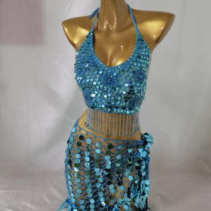 May include: A turquoise blue sequined belly dancing costume with a halter top and a skirt with a fringe. The top has a beaded fringe and the skirt has a net-like design.