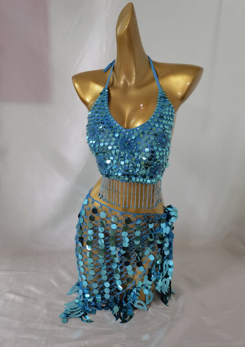 May include: A turquoise blue sequined belly dancing costume with a halter top and a skirt with a fringe. The top has a beaded fringe and the skirt has a net-like design.