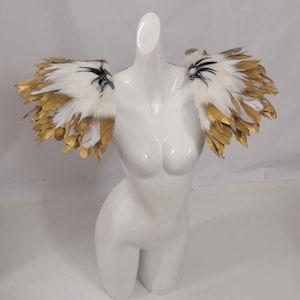 Puede incluir: Un par de hombreras de plumas blancas con detalles dorados. Las plumas est&aacute;n dispuestas en forma de abanico y tienen un aspecto delicado y et&eacute;reo.