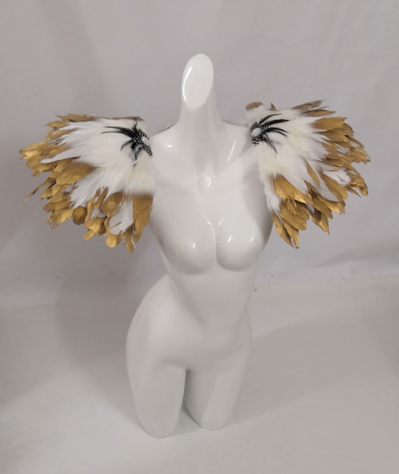 Puede incluir: Un par de hombreras de plumas blancas con detalles dorados. Las plumas est&aacute;n dispuestas en forma de abanico y tienen un aspecto delicado y et&eacute;reo.