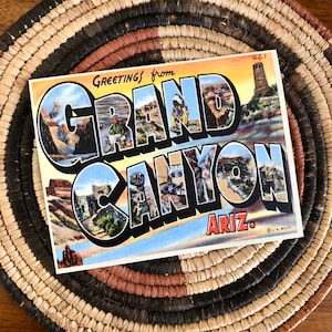 May include: Vintage postcard with a colorful illustration of the Grand Canyon, Arizona. The postcard features the words "Greetings from Grand Canyon Ariz." in a bold, stylized font.