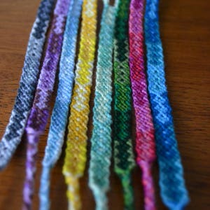 Pode incluir: Uma cole&ccedil;&atilde;o de oito pulseiras de amizade coloridas feitas com fio tecido. As pulseiras s&atilde;o em tons de azul, verde, roxo, amarelo e rosa.