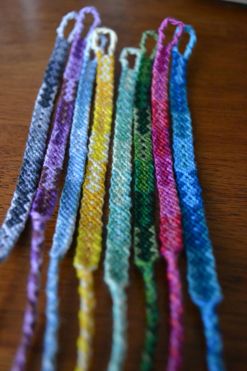 Pode incluir: Uma cole&ccedil;&atilde;o de oito pulseiras de amizade coloridas feitas com fio tecido. As pulseiras s&atilde;o em tons de azul, verde, roxo, amarelo e rosa.
