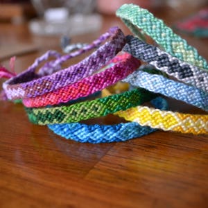 Pode incluir: Um conjunto de pulseiras de amizade coloridas em v&aacute;rios padr&otilde;es, incluindo verde, azul, amarelo, rosa e roxo.