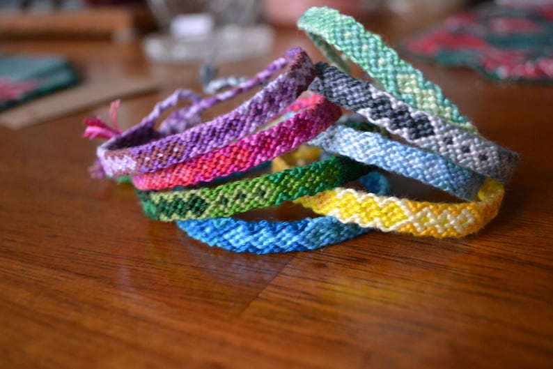 Pode incluir: Um conjunto de pulseiras de amizade coloridas em v&aacute;rios padr&otilde;es, incluindo verde, azul, amarelo, rosa e roxo.