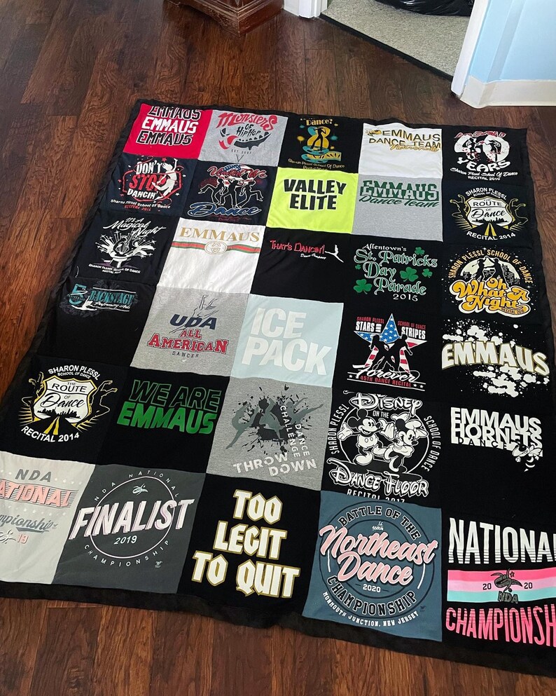 May include: A patchwork quilt made from t-shirts, with a black border. The t-shirts feature text and graphics related to dance and competitions. The quilt is a collection of memories, with a black backing.