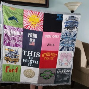 May include: A memory quilt constructed from various colorful t-shirt panels featuring diverse graphic prints, including text such as A-CHAMPS '06, FORD 09, SENIORS 2014, THIS IS WORTH IT, GWYNEDD-MERCY COLLEGE, and Springfield Spartans States Team 2014.