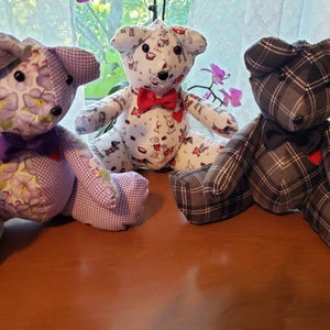 May include: Three handmade teddy bears, one with a purple and white floral pattern, one with a white and black dog pattern, and one with a gray plaid pattern. Each bear is wearing a bow tie.