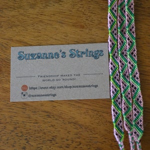 Pu&ograve; includere: Tre braccialetti dell'amicizia rosa, verdi e neri con un biglietto da visita che recita "Suzanne's Strings" e "L'amicizia fa girare il mondo!" con un sito web e un account Instagram.