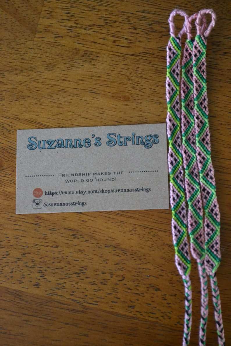 Pu&ograve; includere: Tre braccialetti dell'amicizia rosa, verdi e neri con un biglietto da visita che recita "Suzanne's Strings" e "L'amicizia fa girare il mondo!" con un sito web e un account Instagram.