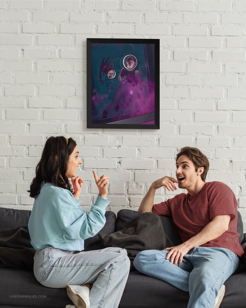 May include: Two people are sitting on a couch and looking at a framed print on the wall. The print is a dark blue background with a person in a purple haze and three circular images of people. The people on the couch are wearing casual clothing.