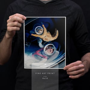 May include: A fine art print featuring an astronaut and a cat in space. The artwork is a vibrant illustration with a blue and white color scheme. The print is 8x10 inches in size and includes the text "FINE ART PRINT" and the artist's website.
