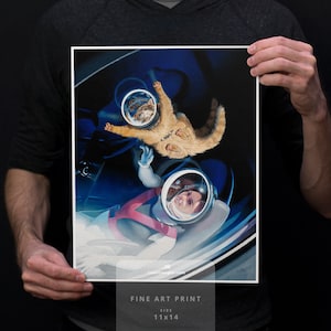 May include: Fine art print featuring a whimsical space scene with a cat and a person in astronaut helmets. The print is 11x14 inches and includes the text "Fine Art Print" and "Size 11x14". The artwork has a blue and white color scheme.