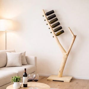 May include: A natural wood wine rack in a tree branch design, holding several wine bottles. The rack is on a wooden base, with a sofa, lamp, and table with wine glasses in the background. The wine rack is a unique home decor item.