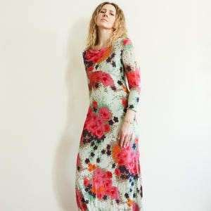 May include: A long-sleeved maxi dress with a floral print in shades of pink, orange, green, and black. The dress has a cowl neck and a fitted silhouette.