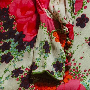 May include: A white fabric with a floral pattern in shades of pink, orange, green, and blue. The fabric has a textured surface and a green trim around the edge.