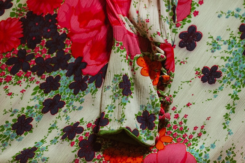 May include: A white fabric with a floral pattern in shades of pink, orange, green, and blue. The fabric has a textured surface and a green trim around the edge.